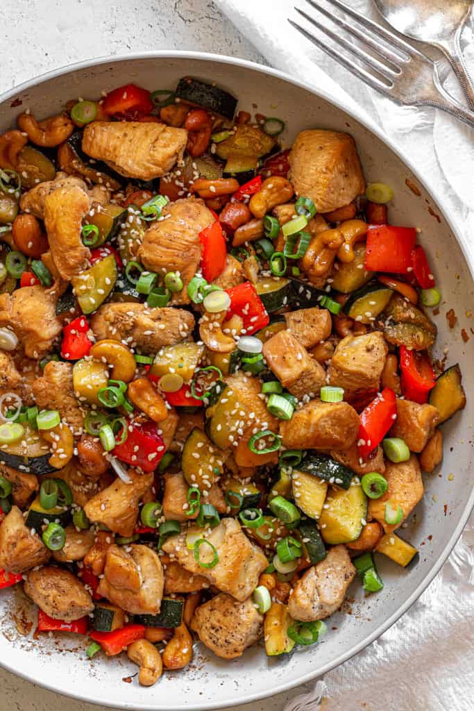 cashew chicken stir fry with red bell peppers, green onions, and green zucchini, topped with sesame seeds