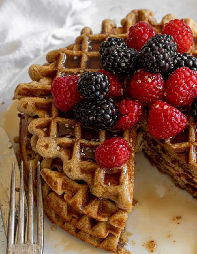 oat waffles cut, topped with maple syrup, blackberries, hemp seeds, and raspberries 